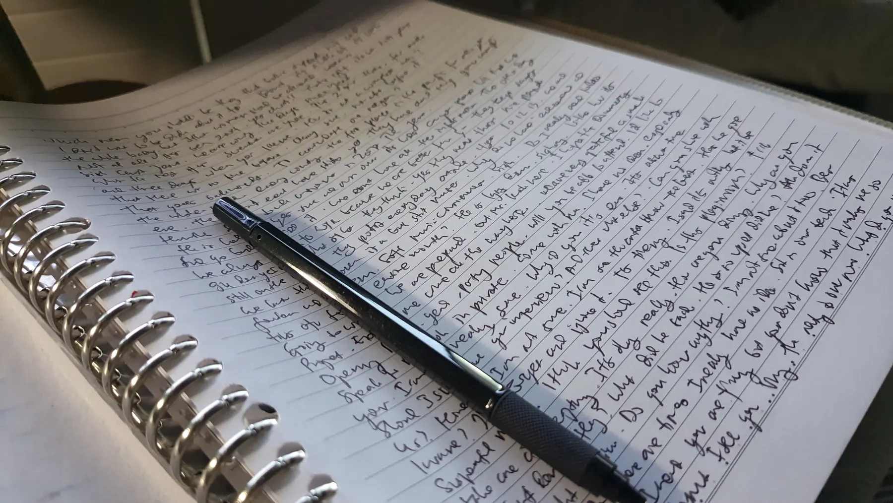 A spiral notebook covered edge to edge in longhand, a pen resting on the page