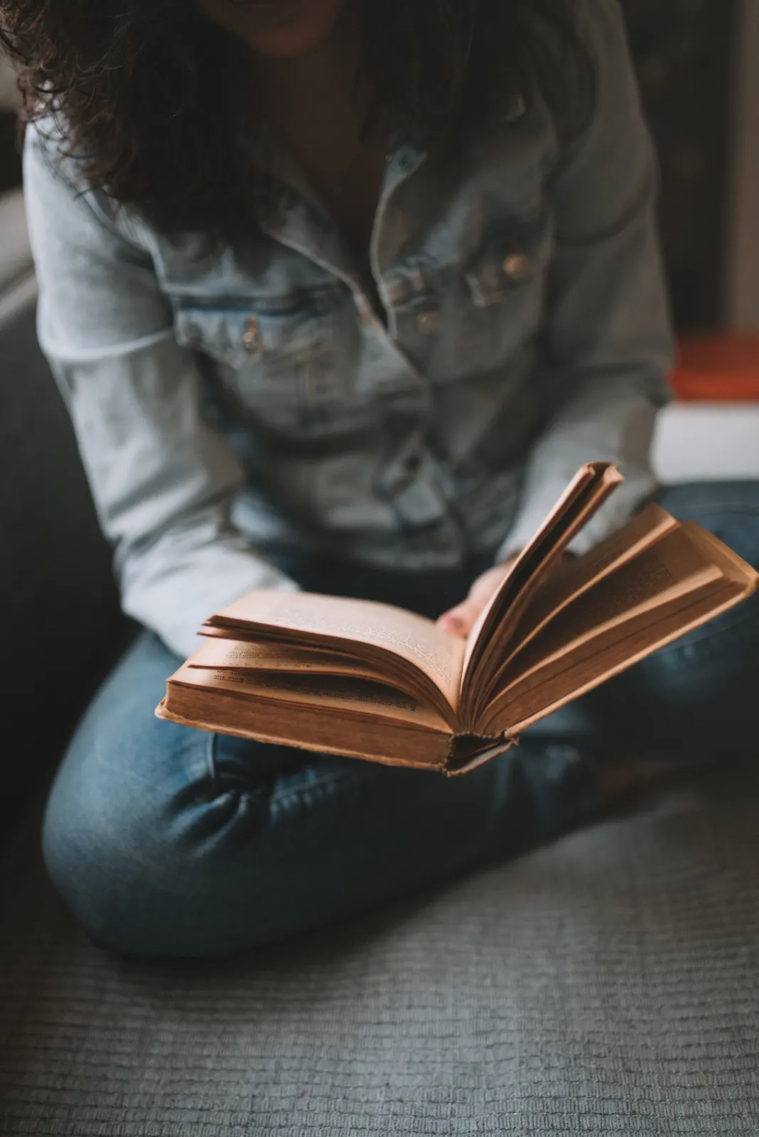 A reader curled on a couch with a well-thumbed paperback open on her lap