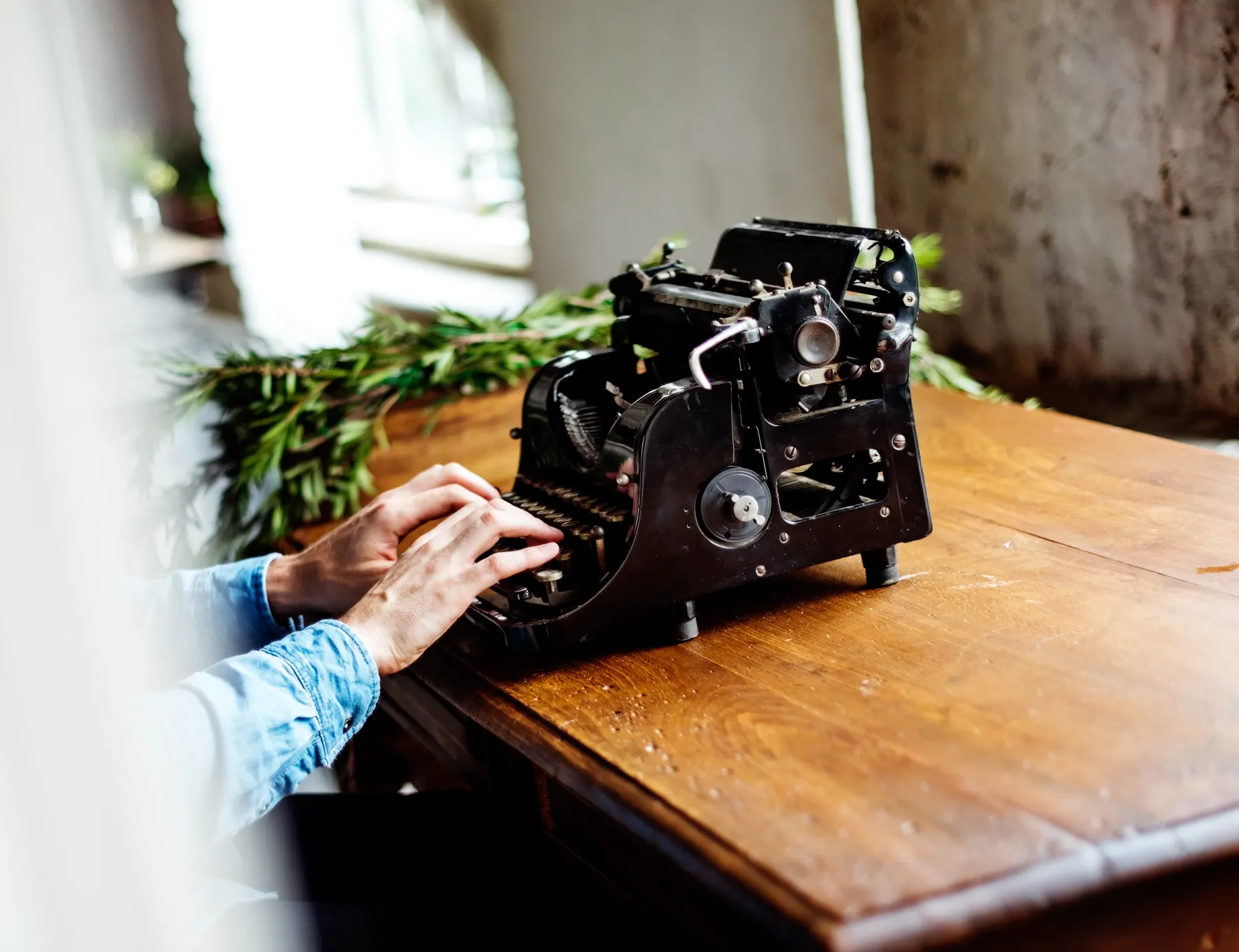 Hands resting on the keys of an old black typewriter on a wooden table