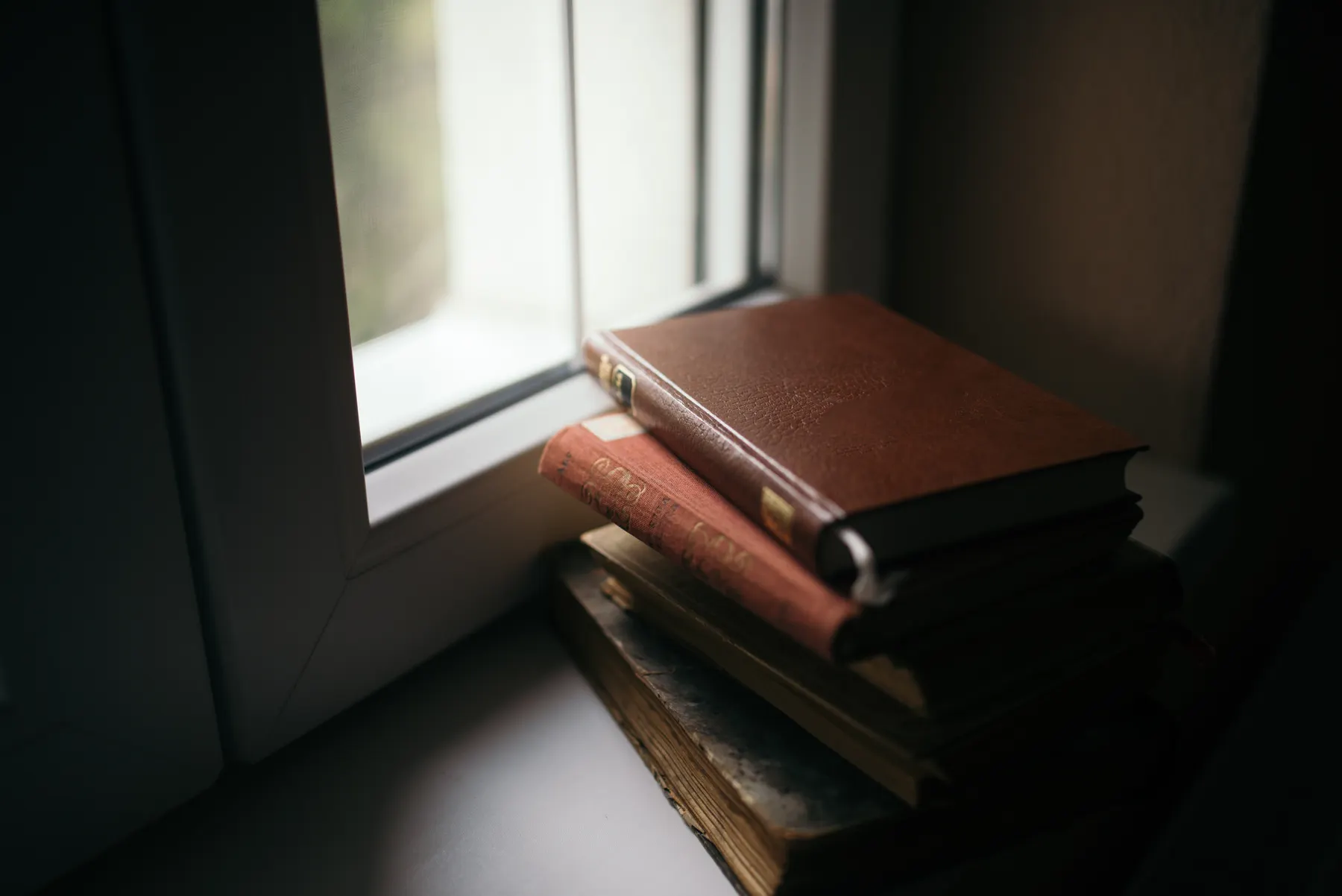 A stack of worn hardback novels on a windowsill in late afternoon light